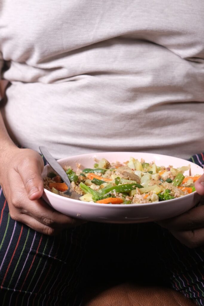 Individual sitting on a couch holding a bowl of vegetable salad, showcasing a healthy lifestyle.